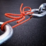 A red cord ties together metal chain links, showing fragile infrastructure
